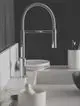 Küchenarmatur in Chrom mit flexibler Feder und Auslauf, montiert auf einer weißen Arbeitsplatte, neben Geschirr und Besteckhaltern. Ideal Standard Produkt.